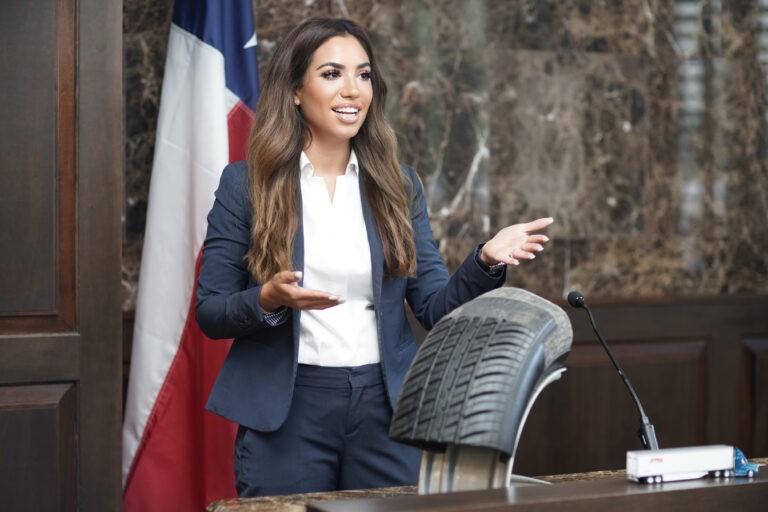 Female trial attorney presenting legal arguments in a courtroom with a Texas flag in the background.