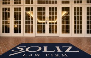 Front entrance of Soliz Law Firm's Houston office, featuring glass French doors and a navy welcome mat with the firm's logo